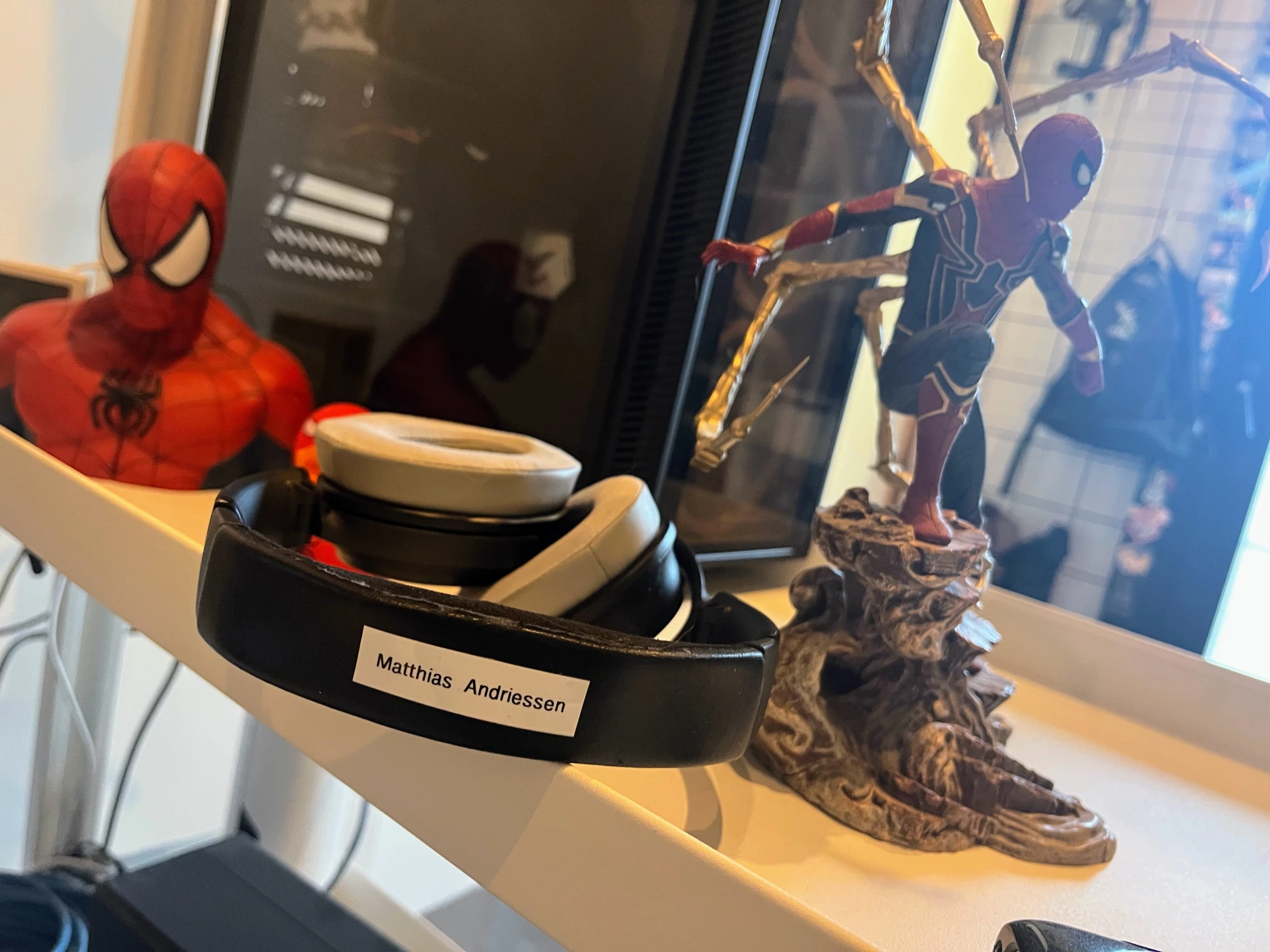 Een headset met de naam "Matthias Andriessen" op, tussen een Spider-Man buste en een Spider-Man beeldje